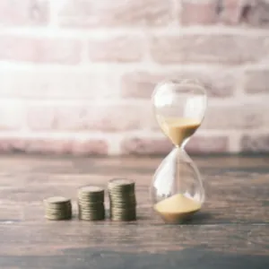 Ampulheta ao lado de pilhas de moedas crescentes, simbolizando economia de tempo e dinheiro
